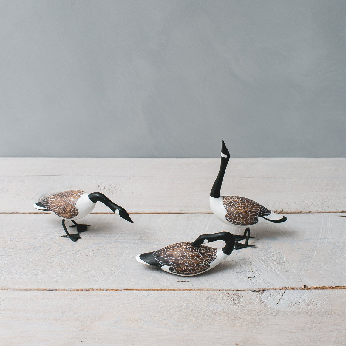 Decorative Canada goose figurines on a wooden surface with a gray background
