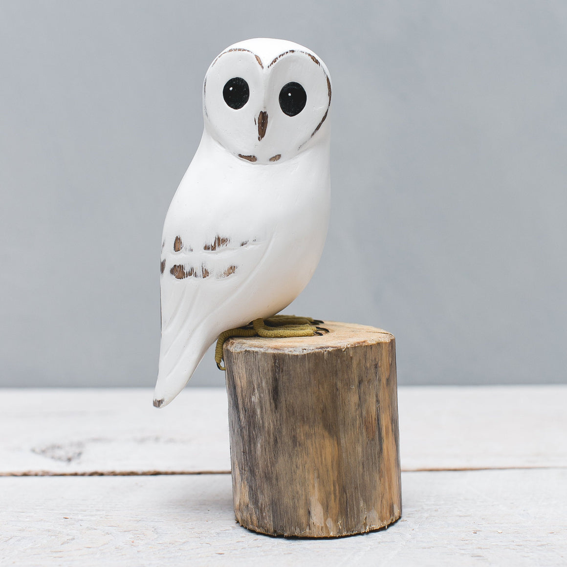 White Barn owl figurine on a wooden stump against a light gray background