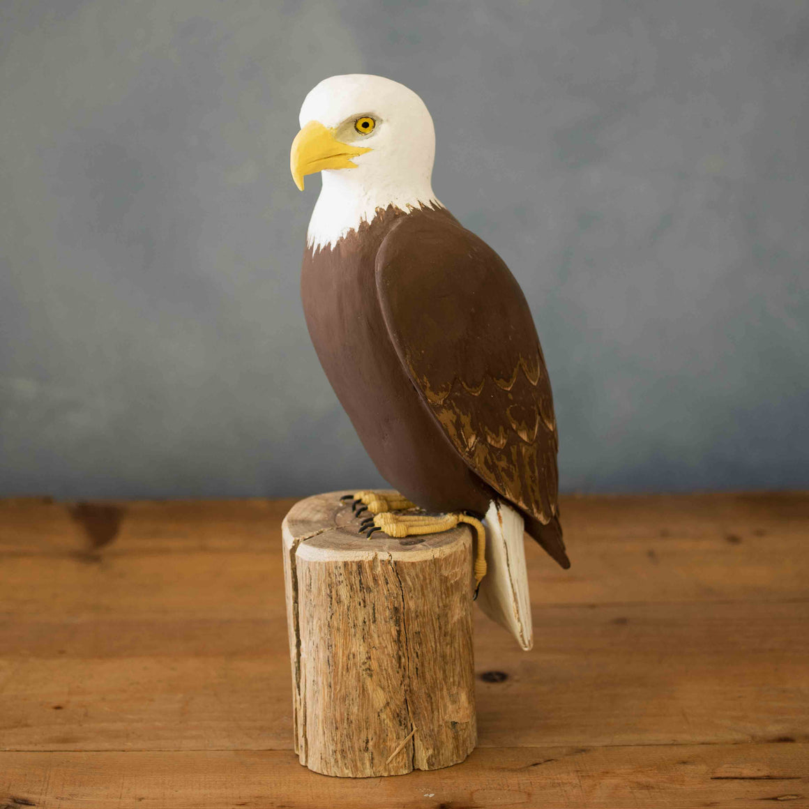 Model of a bald eagle perched on a wooden stump against a gray background