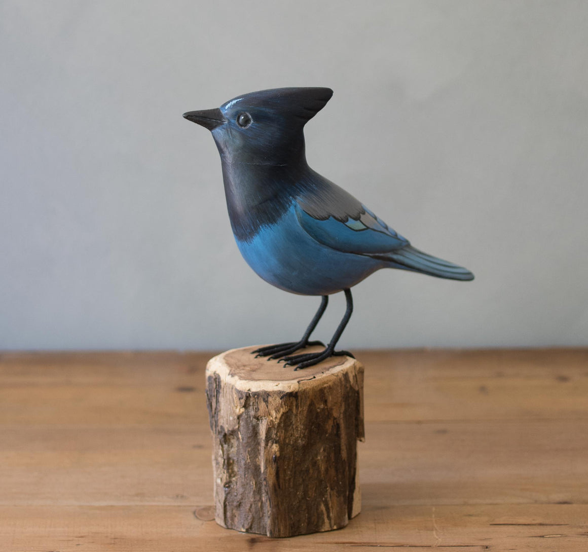 stellers jay Blue bird figurine on a wooden stump against a plain background
