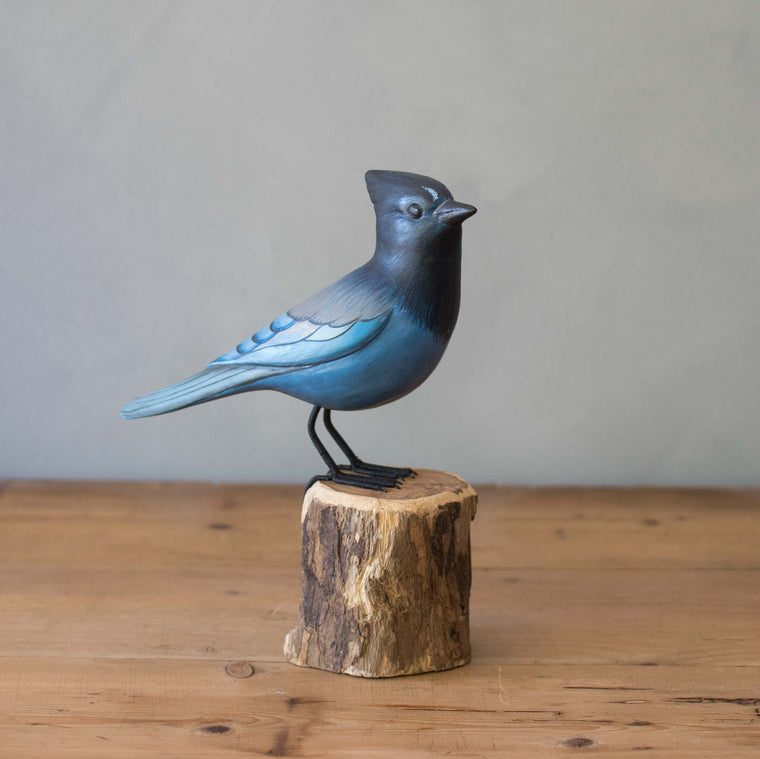Steller's Jay Blue bird figurine on a wooden stump against a gray background